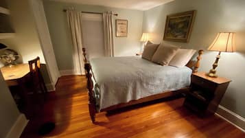 A bedroom with a wooden bed, a nightstand with a lamp, a chair, and a door with curtains.