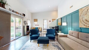 Un salon spacieux doté d’une grande fenêtre, d’un mur d’accent de couleur turquoise et d’un coin salon confortable avec des fauteuils bleus et un canapé beige.