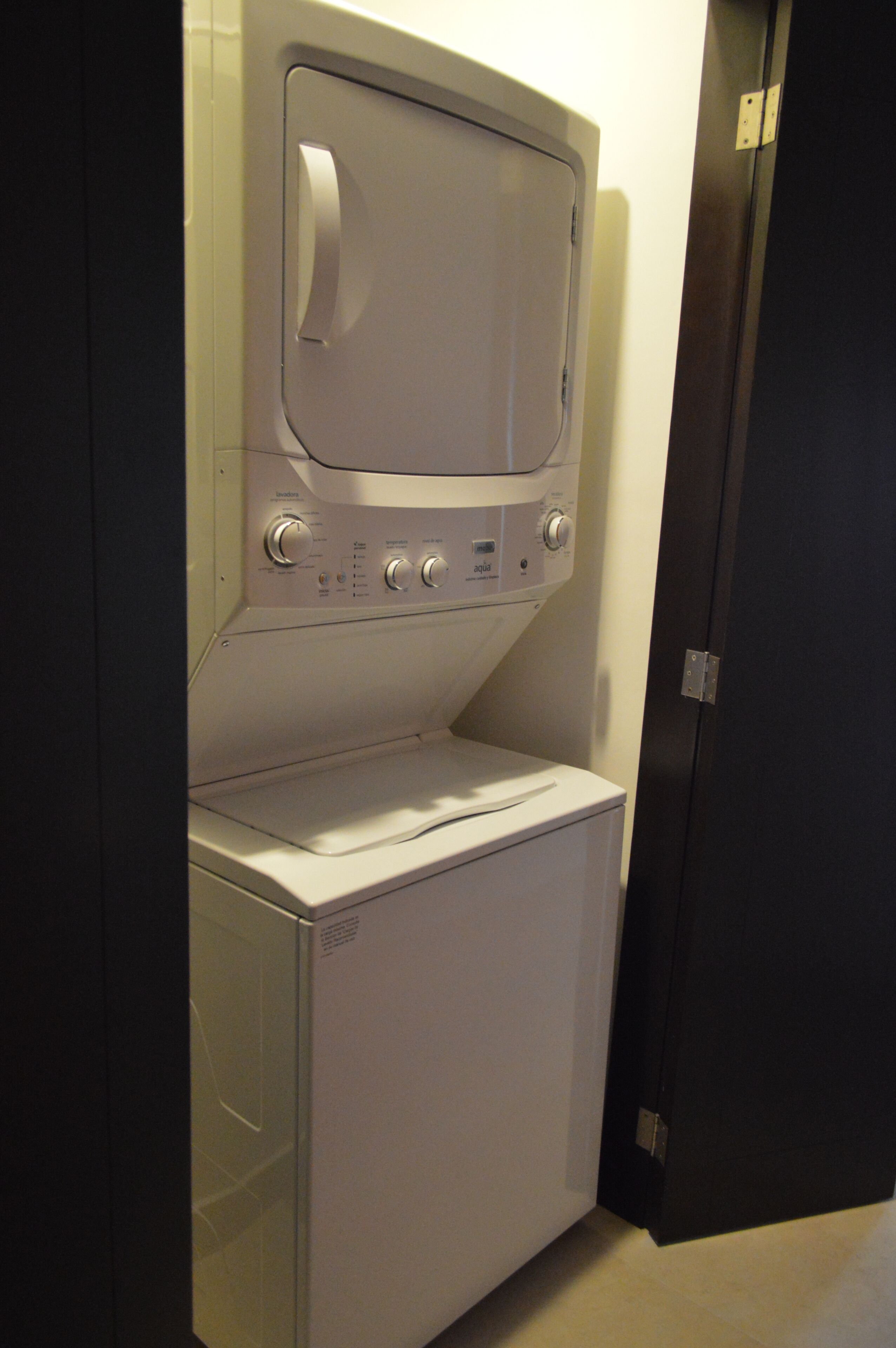 A compact, white washer and dryer unit in a small laundry room with a dark door.