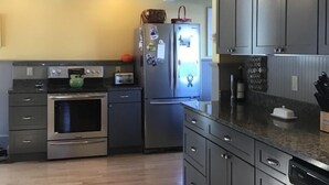 A modern kitchen with grey cabinets, a stainless steel oven, a refrigerator, and a wooden floor. - Historic 1870’s Spacious Home-2 Blocks From Belfast Village and the Bay (Belfast)
