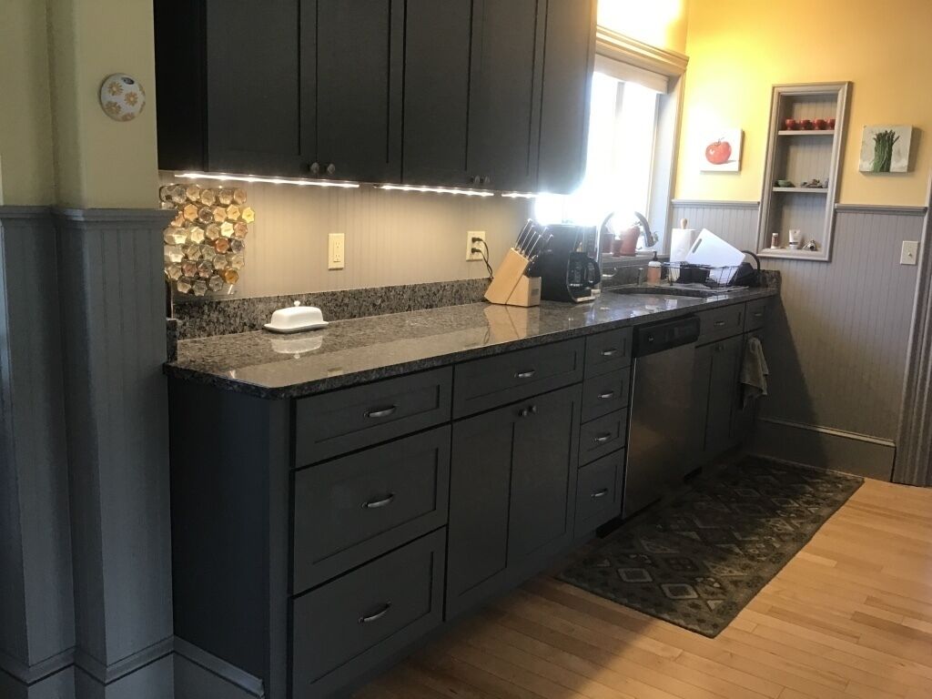 A modern kitchen with dark cabinetry, granite countertops, and a built-in oven.