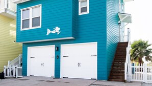 A two-story building with a teal exterior, white railings, and a small balcony. - Serenity Sands Beach HouseFamily-Friendly Ocean View Home (PORT ARANSAS)