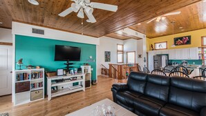 A living room with a black leather sofa, a white entertainment unit, and a teal accent wall. - Serenity Sands Beach HouseFamily-Friendly Ocean View Home (PORT ARANSAS)