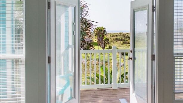A view from a balcony with a wooden deck, white railing, and a clear view of the ocean and distant landscape. - Serenity Sands Beach HouseFamily-Friendly Ocean View Home (PORT ARANSAS)