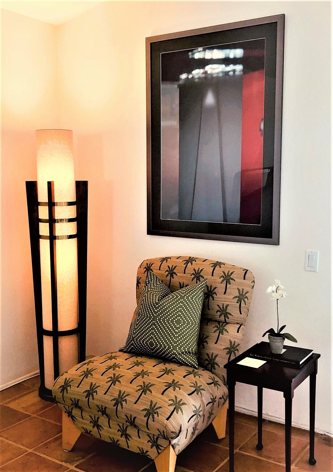 A chair with a palm tree pattern, a tall floor lamp, and a framed picture on the wall.