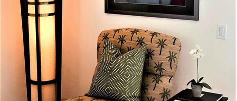 A chair with a palm tree pattern, a tall floor lamp, and a framed picture on the wall.