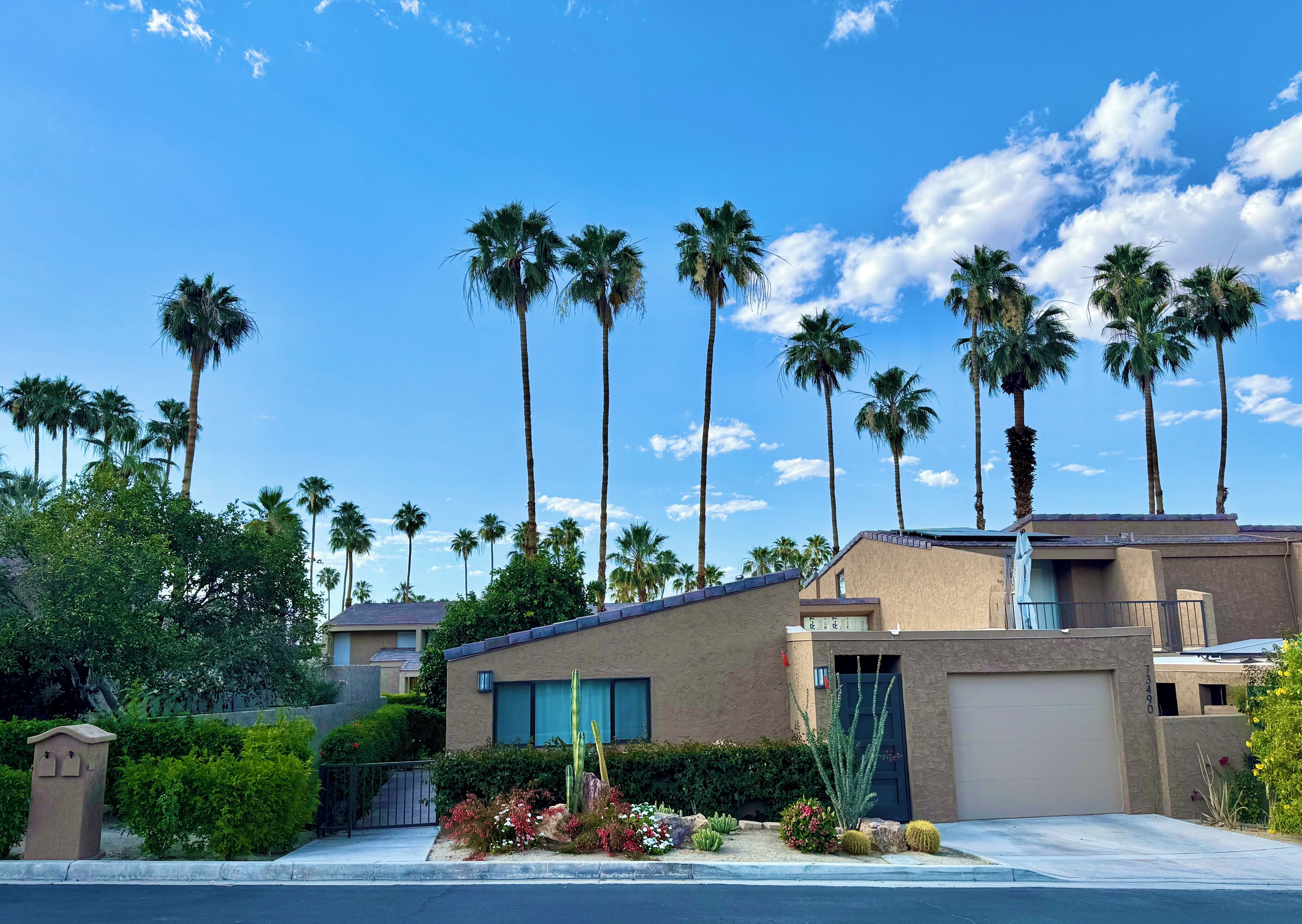 A residential building with a beige exterior, a garage, and a well-maintained garden with cacti and shrubs.