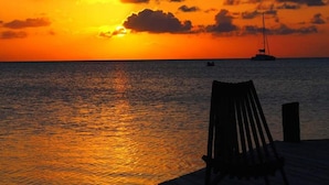 A sunset over the ocean with a chair and a dock. - OCEANSIDE 1ST FLOOR APT, OFF-GRID WITH INFINITY EDGE POOL, DOCK, A/C & SMART TV  (Caye Caulker)