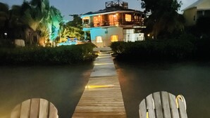A wooden pathway leading to a building with two wooden chairs on either side. - OCEANSIDE 1ST FLOOR APT, OFF-GRID WITH INFINITY EDGE POOL, DOCK, A/C & SMART TV  (Caye Caulker)