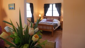 A bedroom with a wooden bed, two windows with curtains, a bedside lamp, and a vase of tulips. - OCEANSIDE 1ST FLOOR APT, OFF-GRID WITH INFINITY EDGE POOL, DOCK, A/C & SMART TV  (Caye Caulker)