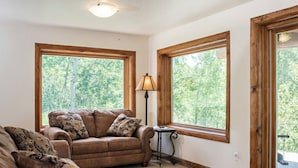 A cozy living room with a brown leather sofa, two large windows with wooden frames, and a small table with a lamp. - Custom Log Cabin w/ MTN Views, 10 min. to fishing! (Basalt)