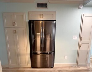 Ein Edelstahl-Kühlschrank in einer Küche mit weißen Schränken und einer hellblauen Wand.