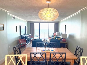 Un espace repas avec une table et des chaises en bois, un lustre et une vue sur l’extérieur.