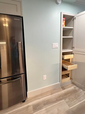 Une cuisine avec un réfrigérateur en acier inoxydable, un meuble en bois doté d’étagères ouvertes et un mur de couleur bleu clair.
