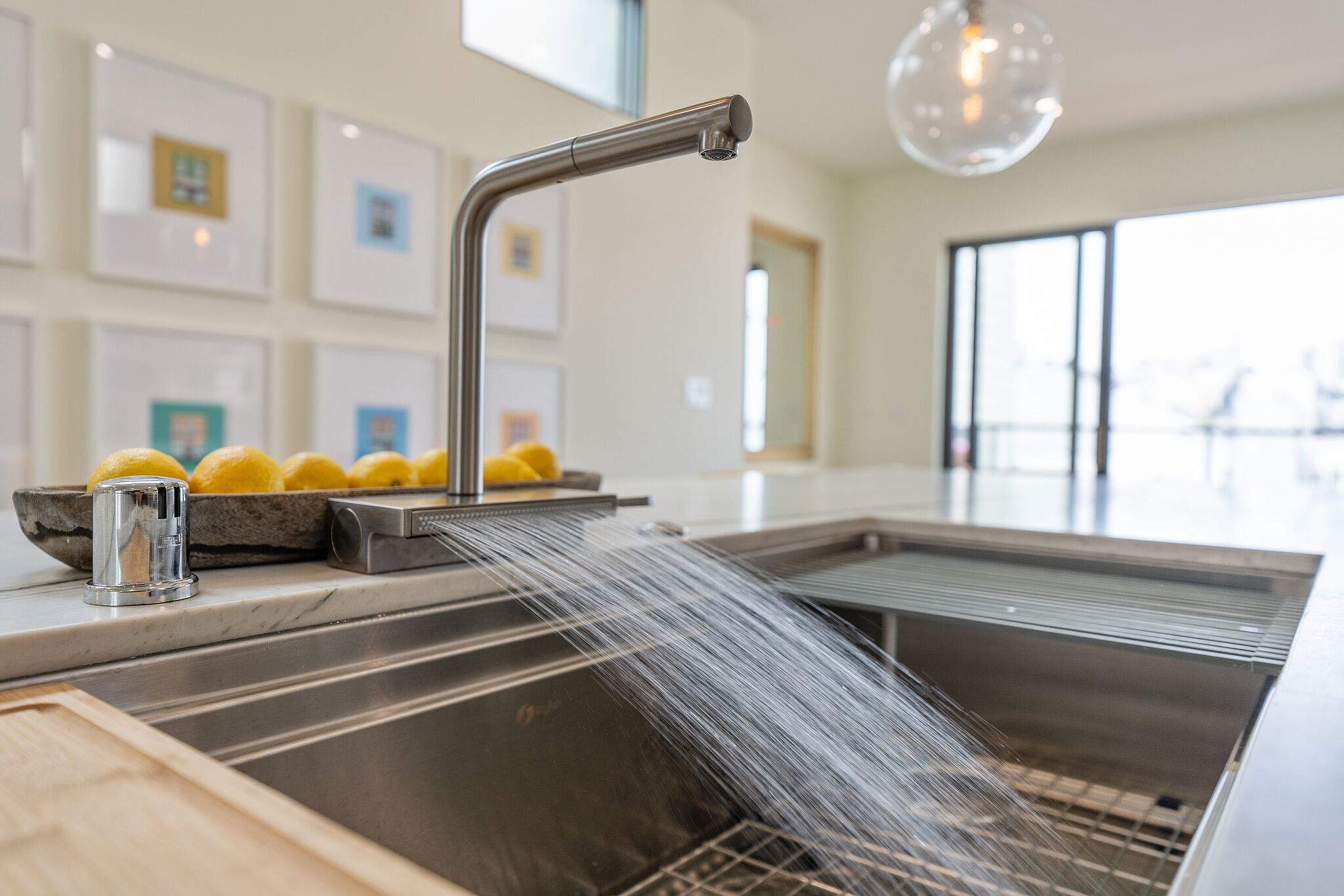 A modern kitchen with a stainless steel sink, a bowl of lemons, and a clear glass light fixture.