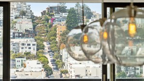 A view from a window with hanging light fixtures, overlooking a densely packed urban street with buildings and parked cars. - Live the Penthouse Dream – Luxe, Views & Vibes in Iconic North Beach (San Francisco)