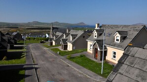 A row of houses with a clear road in front, a grassy area, and a distant view of hills and the sea.