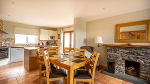 A spacious kitchen with a dining area, featuring a stone fireplace, wooden furniture, and a tiled floor.