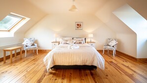 A bedroom with a wooden floor, a bed with a white duvet, two nightstands with lamps, and a window with a view of trees.