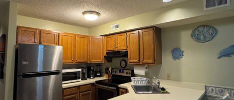 A kitchen with wooden cabinets, stainless steel appliances, a white countertop, and a clock on the wall.