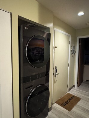 Un lavadero con lavadora y secadora empotradas en la pared, una puerta con felpudo y una lámpara en el techo.