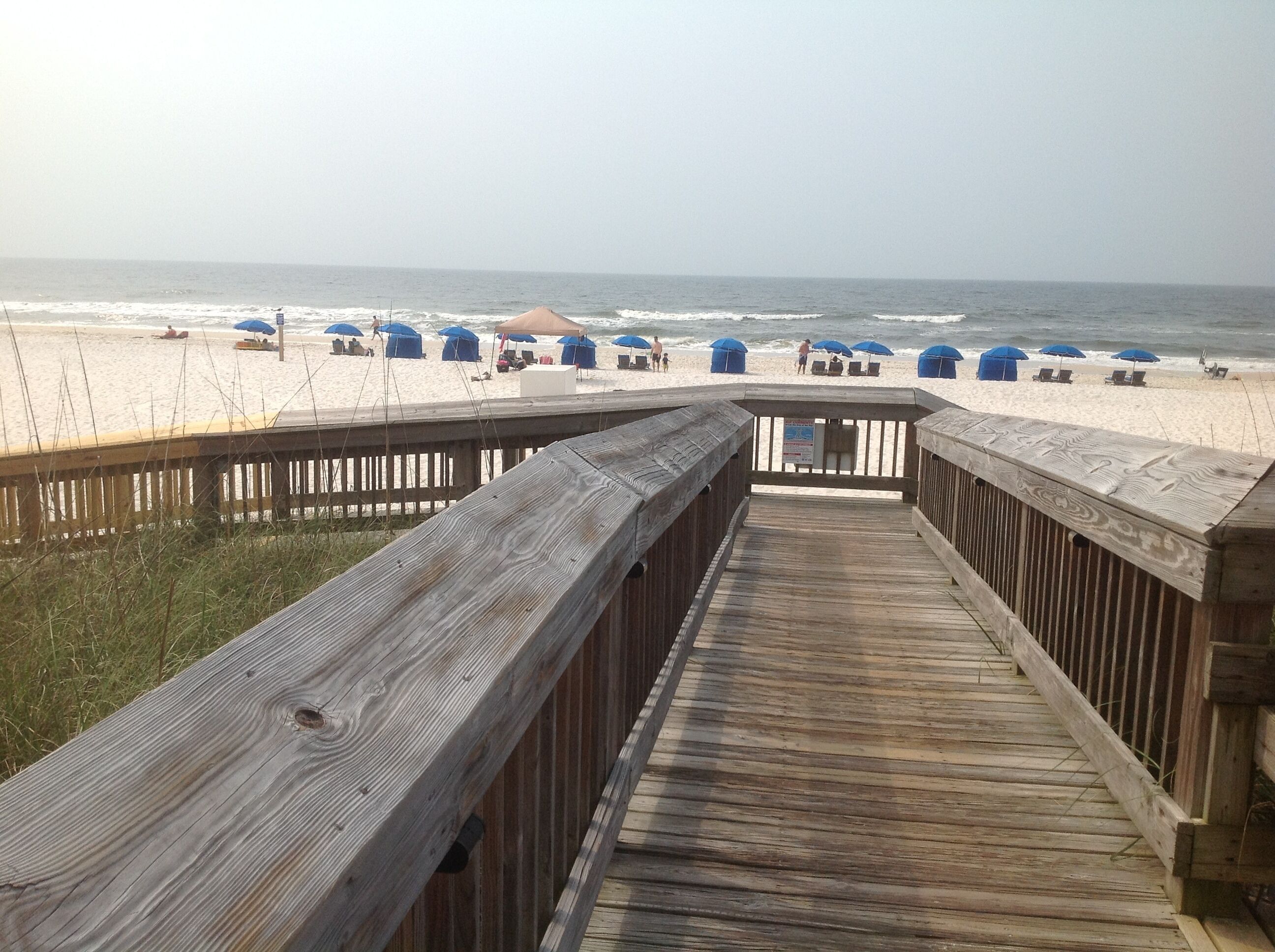 A wooden boardwalk leading to a beach with umbrellas and lounge chairs.