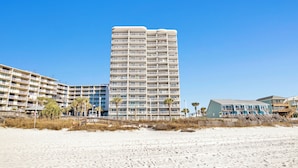 A beachfront hotel with multiple balconies, a sandy beach in the foreground, and a clear blue sky. - NEWLY RENOVATED/DIRECT FRONT/2 BEDROOM CONDO/INDOOR-OUTDOOR POOL/NEAR ATTRACTION (Orange Beach)