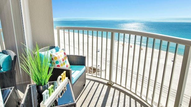 A balcony with a view of a beach, wicker furniture, and a sign that says "BEACH". - NEWLY RENOVATED/DIRECT FRONT/2 BEDROOM CONDO/INDOOR-OUTDOOR POOL/NEAR ATTRACTION (Orange Beach)