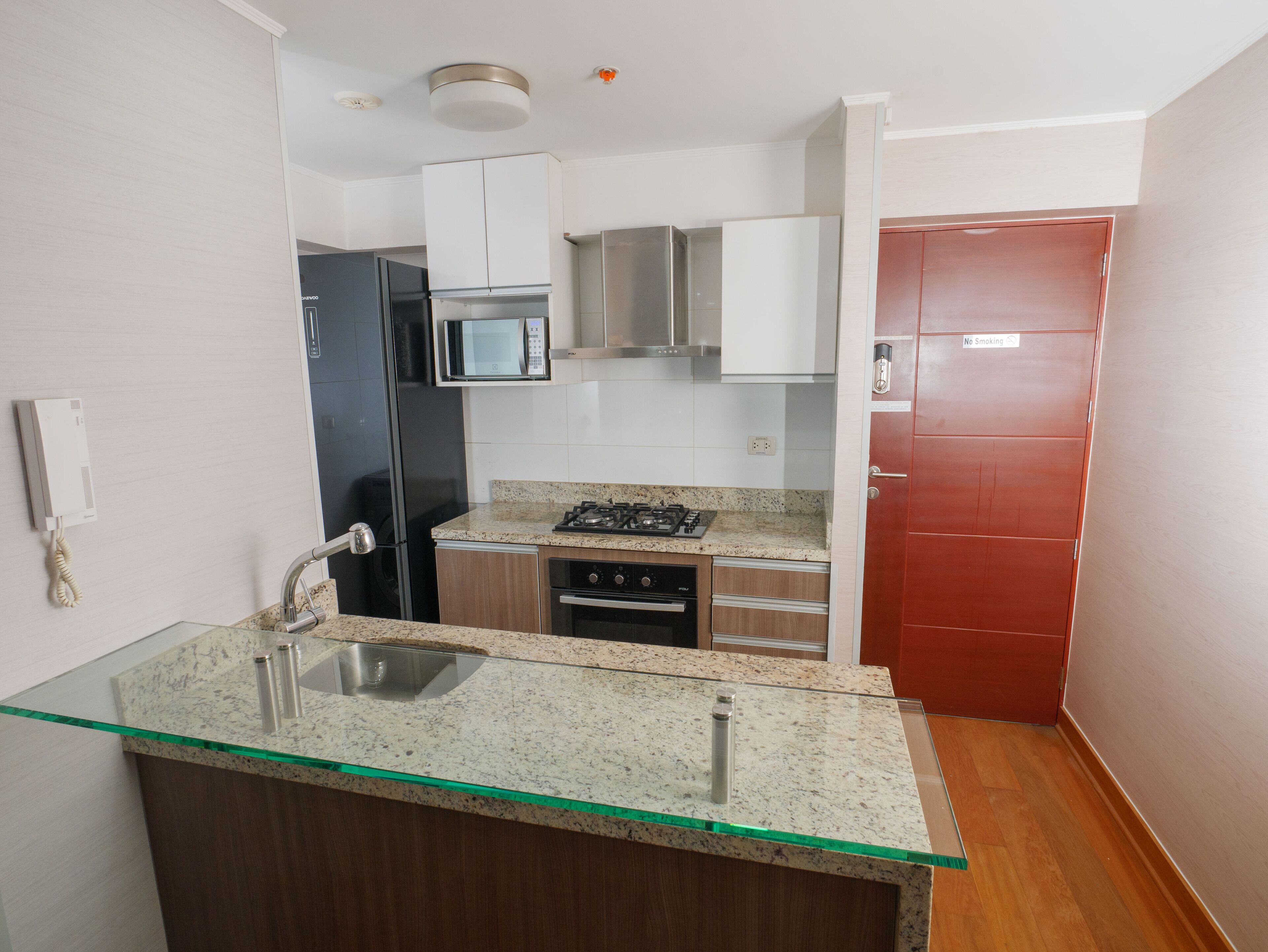 A compact kitchen with a glass-top island, stainless steel appliances, and a red door.