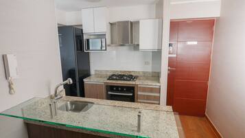 A compact kitchen with a glass-top island, stainless steel appliances, and a red door.