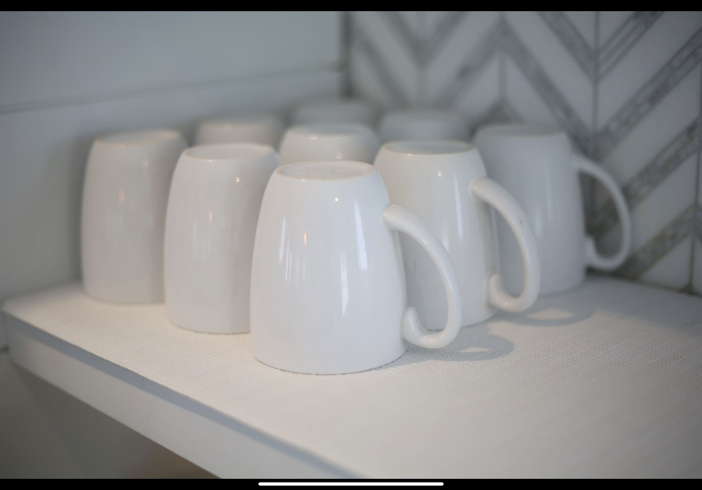 A row of white ceramic mugs on a white shelf.