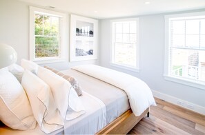 A bedroom with a large bed, multiple pillows, and a view of greenery through the windows.