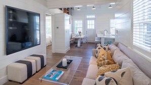A spacious living area with a large flat-screen TV, a sofa with patterned cushions, and a clear glass coffee table. - Luxurious Harbor “Elizabeth” Cottage! Walk & bike to everything (Nantucket)