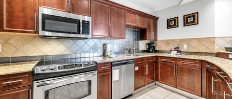A kitchen with wooden cabinets, stainless steel appliances, a tiled backsplash, and granite countertops.