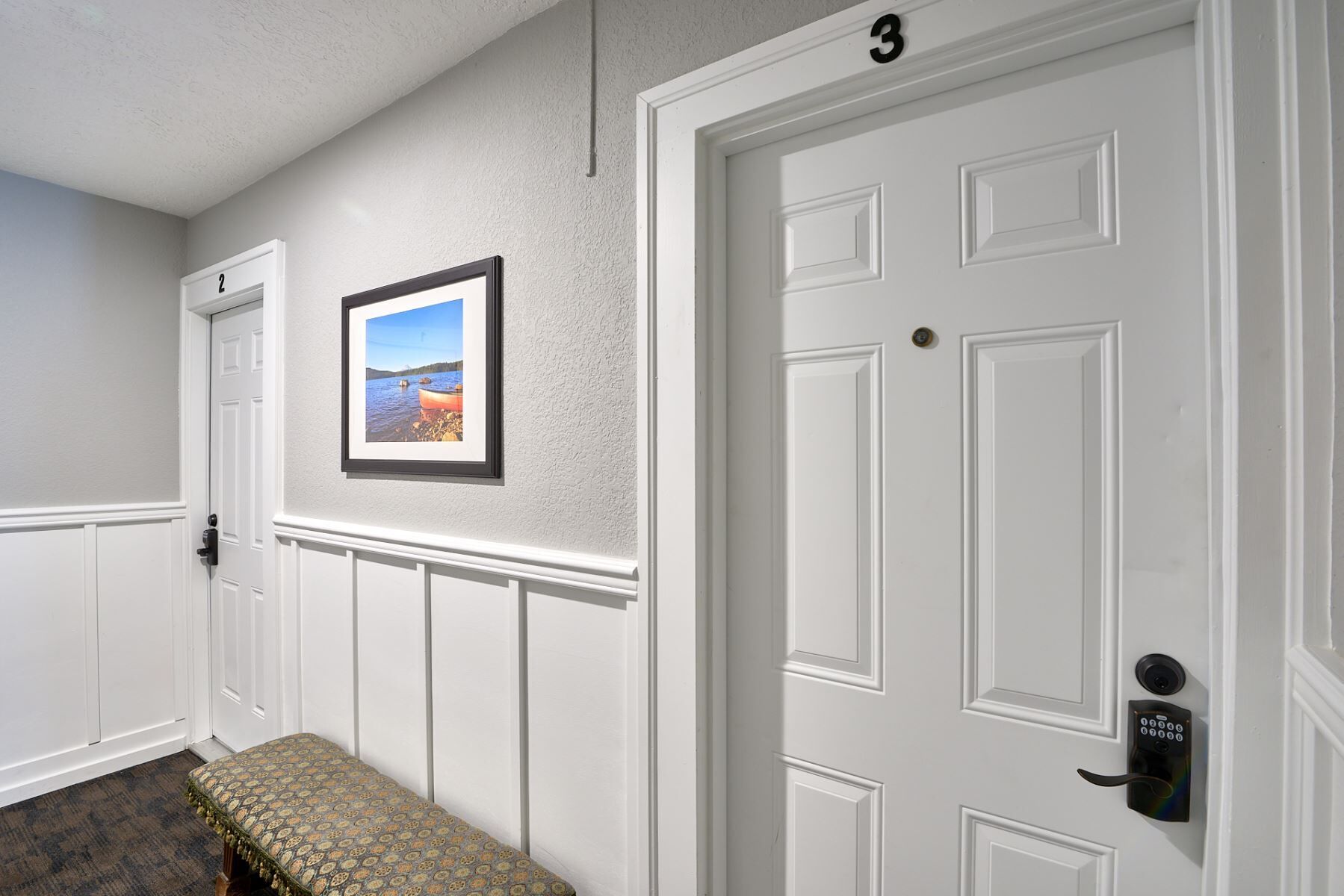A hallway with a bench, a door with a keypad lock, and a framed picture on the wall.