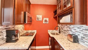 A compact kitchen with wooden cabinets, a microwave, a coffee maker, a sink, and a toaster.