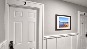 A hallway with white doors numbered 2 and 3, a picture frame on the wall, and a doorbell.