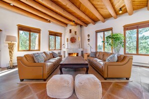 A spacious living room with a fireplace, leather sofas, and a large window. - Spacious traditional Santa Fe adobe home (Santa Fe)