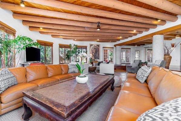 A spacious living room with a wooden ceiling, leather sofas, a coffee table, and large windows. - Spacious traditional Santa Fe adobe home (Santa Fe)