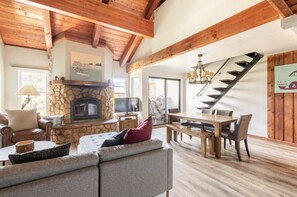 Uma sala de estar ampla com lareira de pedra, vigas de madeira, área de jantar e escada.