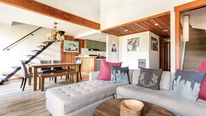 A modern living room with a grey sectional sofa, wooden coffee table, and a staircase leading to an upper floor.