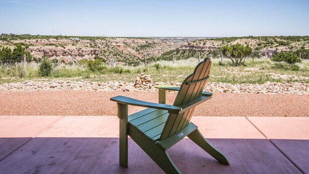 A green Adirondack chair on a wooden deck overlooking a rugged landscape with rocky hills and sparse vegetation.
