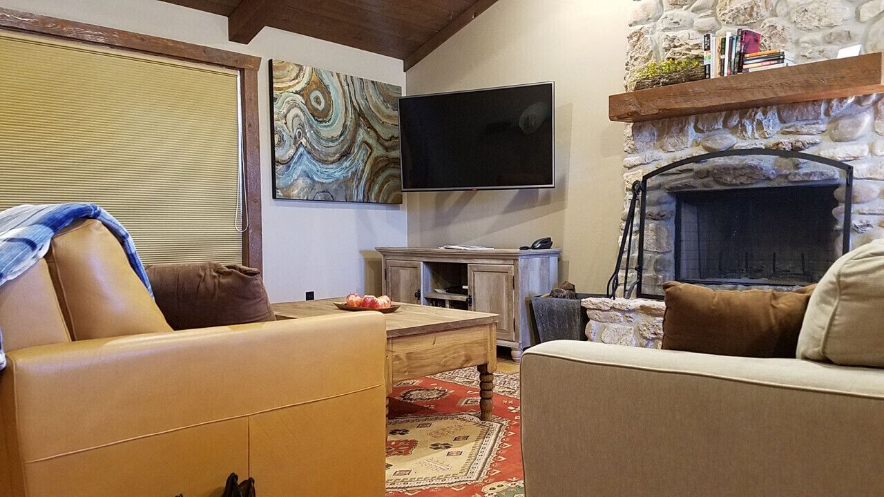 Ein gemütliches Wohnzimmer mit Kamin aus Stein, einem flachbildfernseher darüber und einem bequemen Sofa.