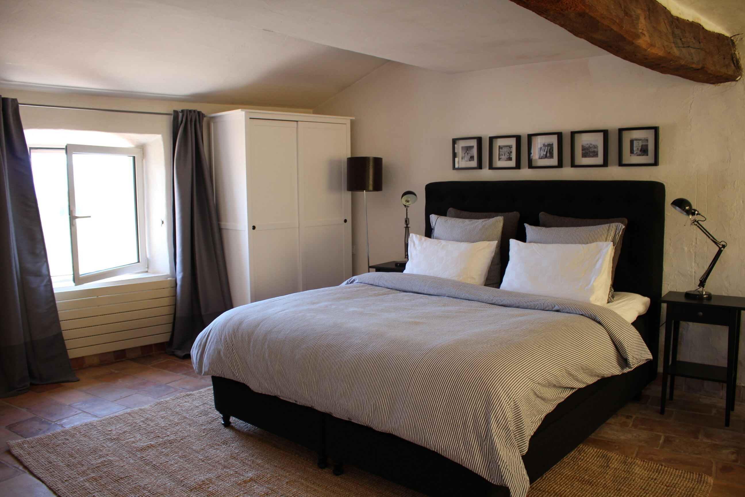 Une chambre à coucher avec un grand lit, une armoire, une table de chevet avec une lampe et une fenêtre avec des rideaux.