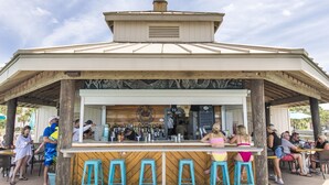 Un bar exterior con estructura de madera, taburetes de bar y una barra con un panel de menú.