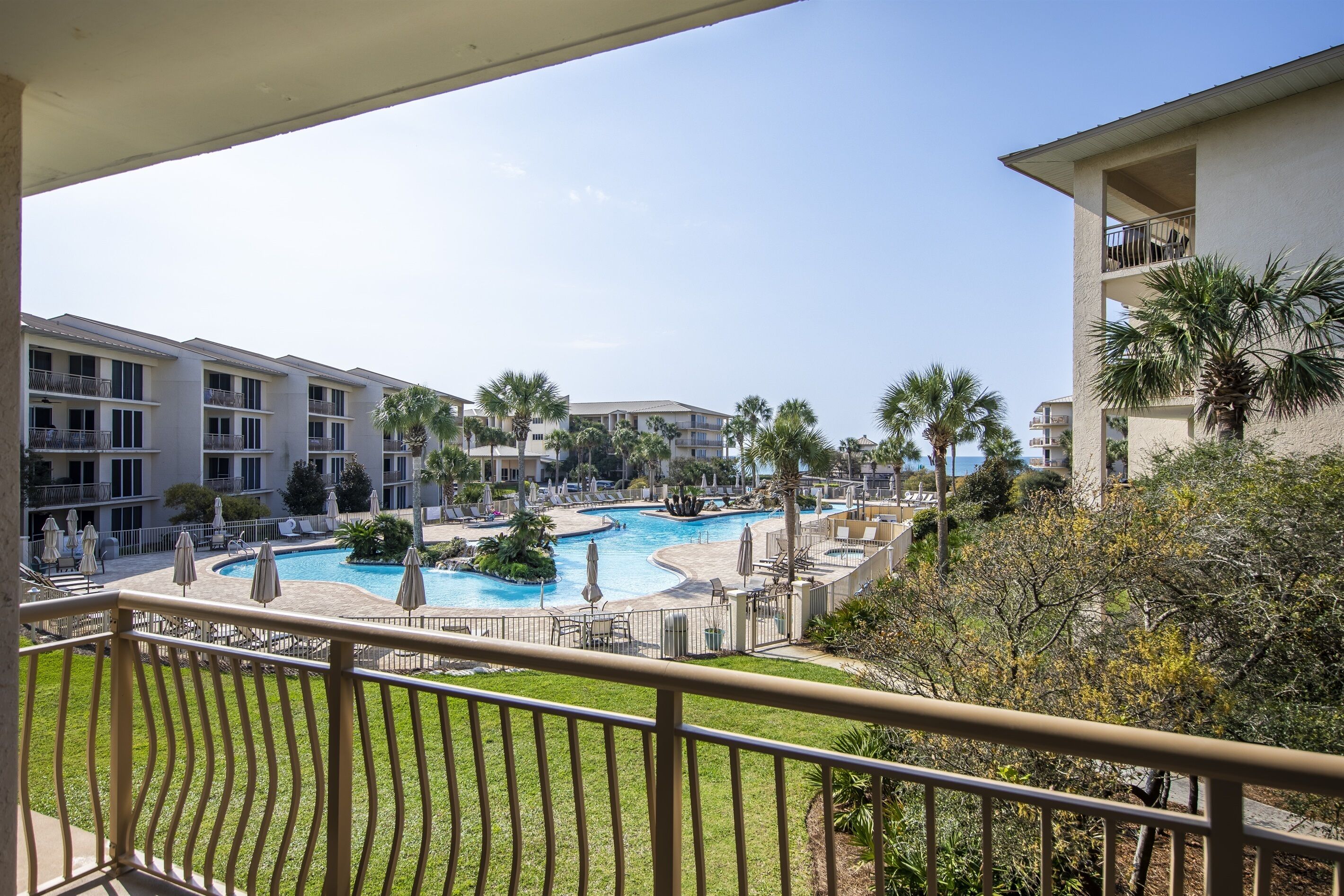 A hotel with a pool area, including lounge chairs and umbrellas, surrounded by palm trees and a clear sky.
