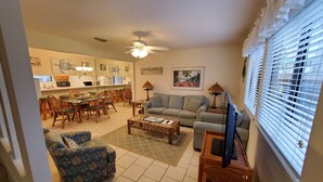 A living room with a sofa, armchair, and coffee table. There is a dining area with chairs and a table. A ceiling fan is visible, and the room has a window with blinds. - Paradise On The Beach With Crystal Clear Water & Gulf Front Complex--2 BR Suites (Navarre)