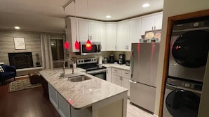 A modern kitchen with white cabinets, a large island, stainless steel appliances, and pendant lighting.