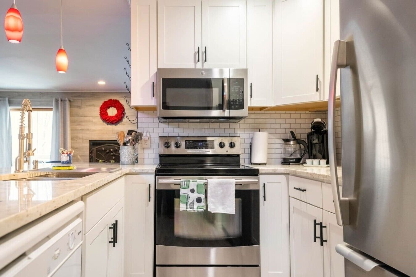 Una cocina moderna con electrodomésticos de acero inoxidable, armarios blancos e iluminación colgante.