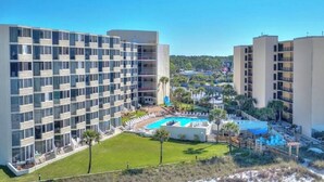 A hotel with multiple floors, a swimming pool, and a landscaped area with palm trees. - Beautiful Beachfront Studio with Beach Chairs for 2 (Panama City Beach)